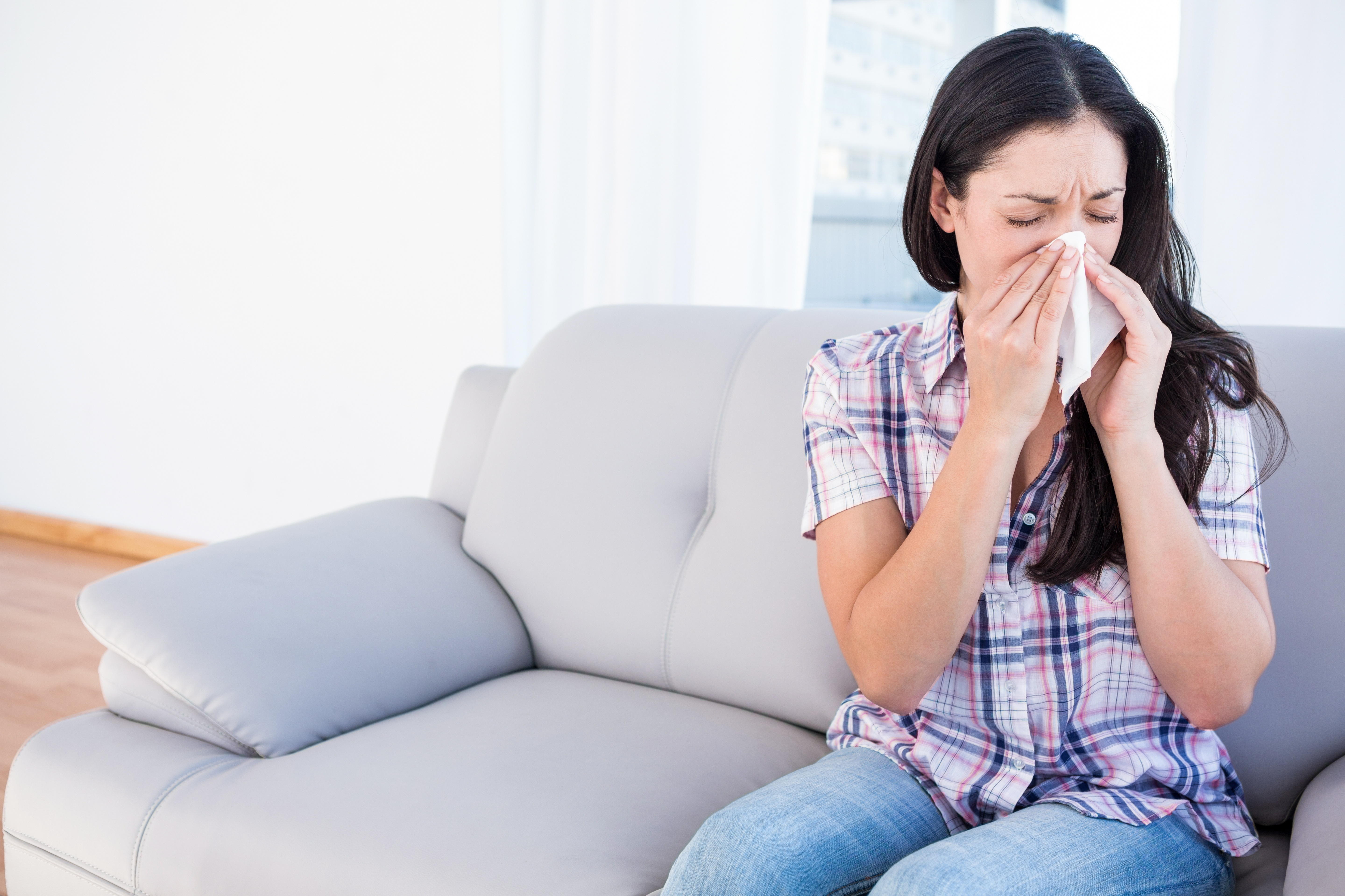 woman sneezing in tissue on couch