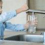 A little girl pouring herself a glass of water from the tap