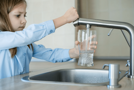 A little girl pouring herself a glass of water from the tap