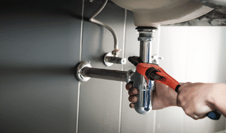 Person performing plumbing maintenance underneath a sink