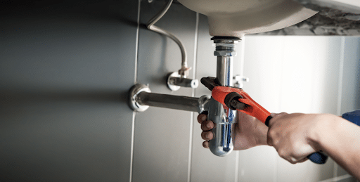 Person performing plumbing maintenance underneath a sink